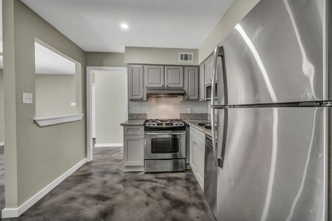 Kitchen featuring stainless steel appliances, gray cabinetry, concrete floors, decorative backsplash, and baseboards | Image 4
