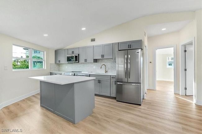 Kitchen featuring stainless steel appliances, gray cabinets, light countertops, a kitchen island, and decorative backsplash - Virtually edited | Image 12