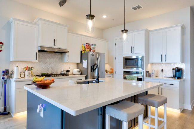 Kitchen featuring light wood-type flooring, visible vents, under cabinet range hood, appliances with stainless steel finishes, and backsplash | Image 25