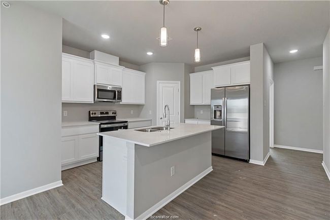 Kitchen featuring stainless steel appliances, sink, white cabinetry, an island with sink, and pendant lighting | Image 6