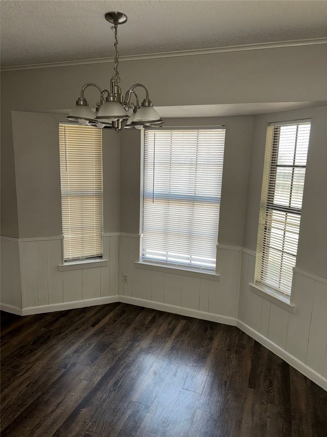 Unfurnished dining area featuring a chandelier, a wainscoted wall, dark wood finished floors, a textured ceiling, and crown molding | Image 7