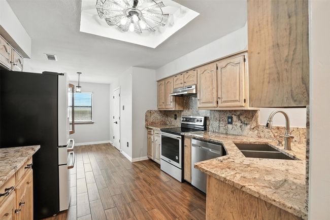 Kitchen with stainless steel appliances, under cabinet range hood, backsplash, and light stone countertops | Image 11