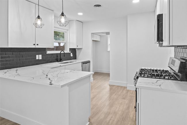 Kitchen with a sink, light stone countertops, white cabinets, baseboards, and light wood-type flooring | Image 11