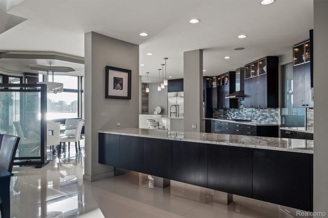 Kitchen with dark cabinets, modern cabinets, decorative light fixtures, glass insert cabinets, and light tile patterned floors | Image 49
