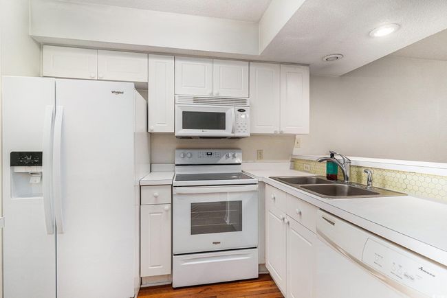 Kitchen with white appliances, a sink, white cabinetry, light countertops, and a textured ceiling | Image 22
