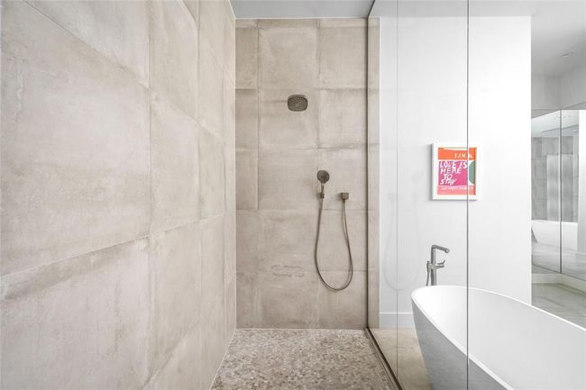 The walk-in shower is wrapped in oversized matte tile and features both a rain shower and handheld spray. A frameless glass enclosure creates a sleek, modern look, while the stone pebble floor adds a spa-like feel underfoot. | Image 20