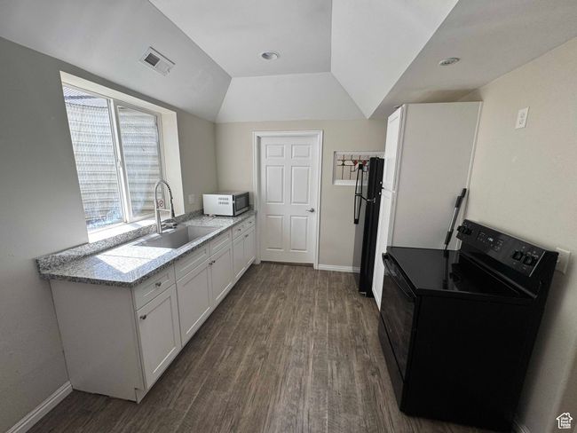 Kitchen with black electric range, a sink, dark wood finished floors, white cabinetry, and light countertops | Image 17