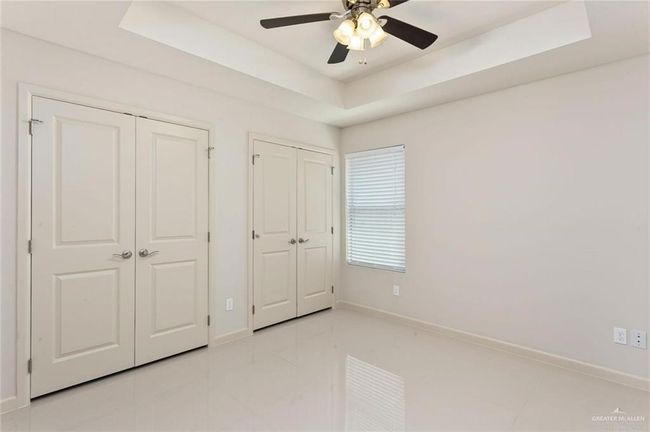 Unfurnished bedroom featuring multiple closets, light tile patterned flooring, a raised ceiling, and a ceiling fan | Image 11