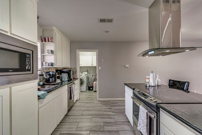 Kitchen with a sink, dark countertops, stainless steel appliances, wall chimney exhaust hood, and washer / dryer | Image 14