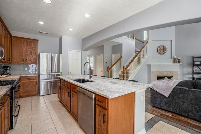 Stepping back toward the breakfast room, this wider view showcases the heart of the home—seamlessly connecting the kitchen, living, and dining areas. The kitchen shines with leathered granite counters, a spacious island with storage, and tall upper cabinets. From here, you can take in the dramatic arched transitions, soaring living room ceilings, and the wall of windows filling the space with natural light. | Image 14