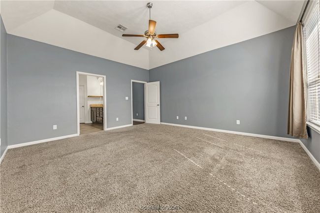 Unfurnished bedroom featuring ceiling fan, ensuite bath, vaulted ceiling, and carpet | Image 25