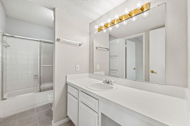 Full bath with tile patterned floors, toilet, vanity, a textured ceiling, and shower / bath combination with glass door | Image 9