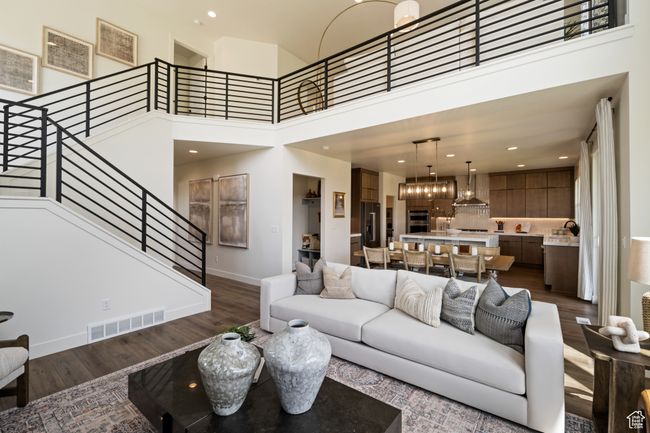 Living room with dark wood-style floors, stairs, baseboards, a high ceiling, and recessed lighting | Image 4