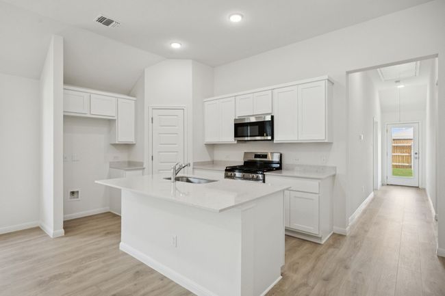 Kitchen featuring stainless steel appliances, white cabinetry, light wood-style flooring, light countertops, and a kitchen island with sink | Image 8