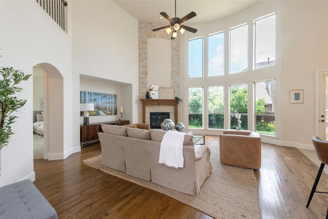 Living area featuring a towering ceiling, healthy amount of natural light, a ceiling fan, a stone fireplace, and wood finished floors | Image 9