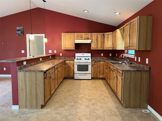 Kitchen with white range with gas stovetop, a sink, lofted ceiling, a peninsula, and under cabinet range hood | Image 6