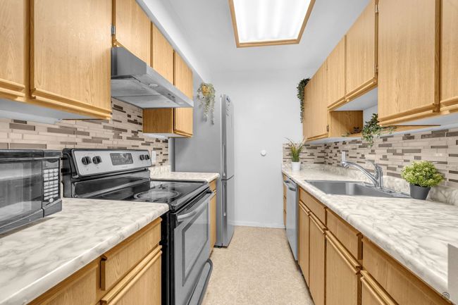 Kitchen featuring light countertops, baseboards, appliances with stainless steel finishes, under cabinet range hood, and a sink | Image 20