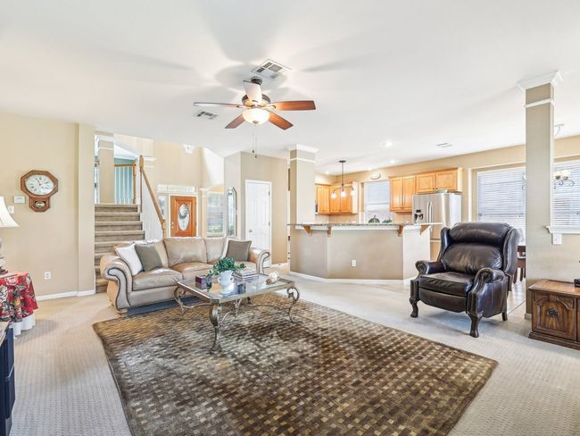 Living room featuring decorative columns, light carpet, a ceiling fan, stairs, and baseboards | Image 5