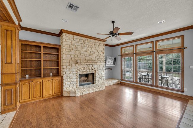 Unfurnished living room with a ceiling fan, ornamental molding, a textured ceiling, light wood-type flooring, and a stone fireplace | Image 13