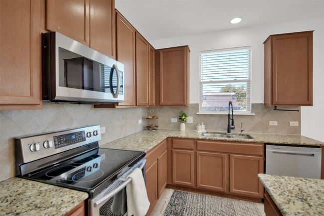 Kitchen with decorative backsplash, brown cabinets, light stone countertops, stainless steel appliances, and a sink | Image 15