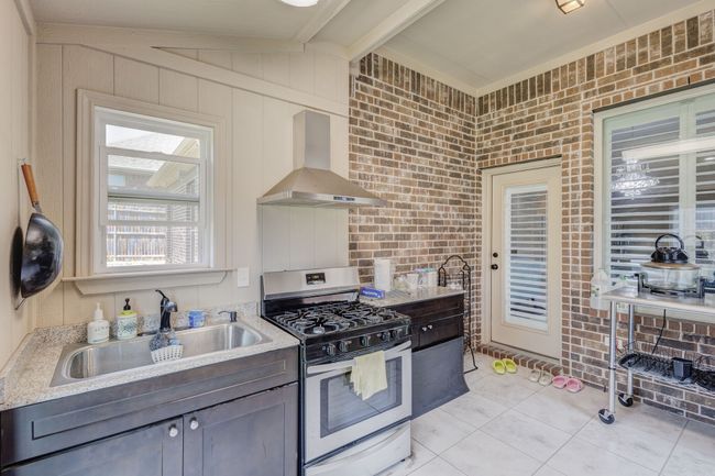 Kitchen with wall chimney range hood, stainless steel range with gas cooktop, a sink, light tile patterned floors, and beam ceiling | Image 29