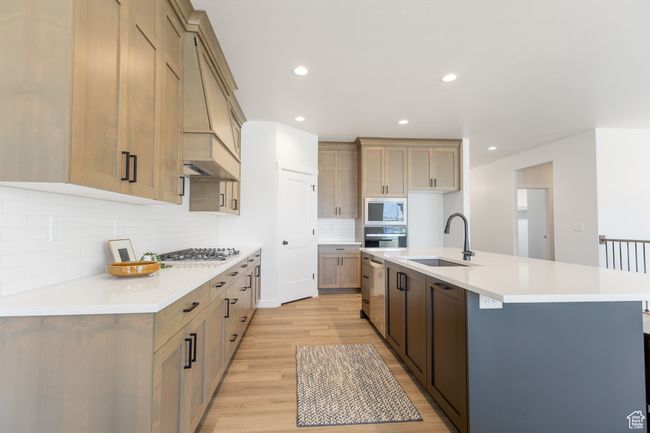 Kitchen with stainless steel appliances, a sink, light wood finished floors, tasteful backsplash, and a center island with sink | Image 6