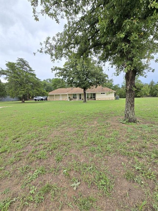 Back view of this charming single-story home set on a spacious, grassy lot with mature trees. Ideal for privacy and outdoor activities. | Image 5