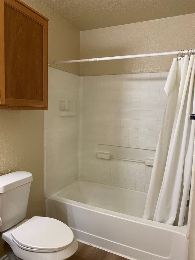 Bathroom with a textured wall, shower / tub combo, toilet, wood finished floors, and a textured ceiling | Image 13