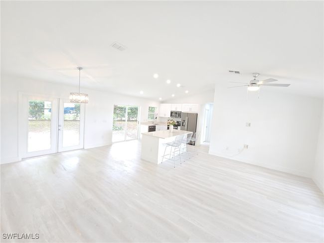 Unfurnished living room featuring vaulted ceiling, baseboards, a chandelier, ceiling fan, and light wood-style flooring | Image 17