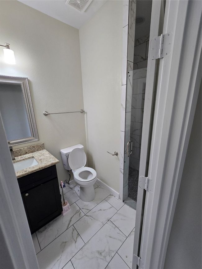 Full bath with a shower stall, marble look tile flooring, vanity, and toilet | Image 13