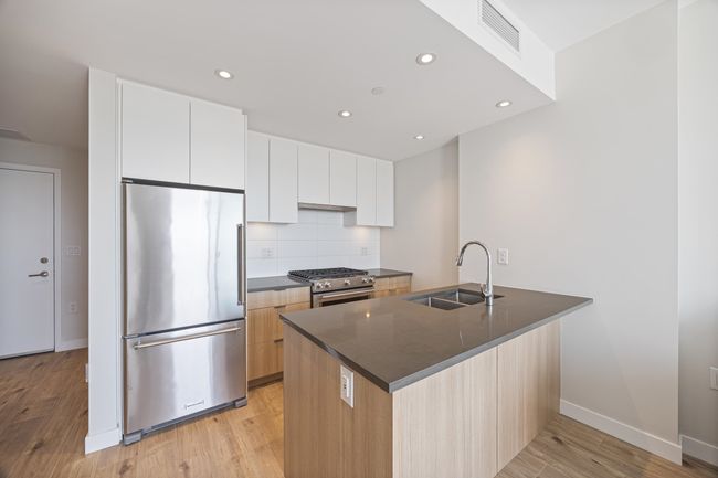 Kitchen with visible vents, stainless steel appliances, dark countertops, a sink, and light wood-type flooring | Image 5