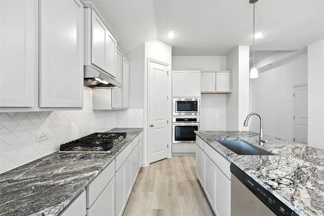 Kitchen with stainless steel appliances, under cabinet range hood, decorative backsplash, light wood-type flooring, and stone counters | Image 5