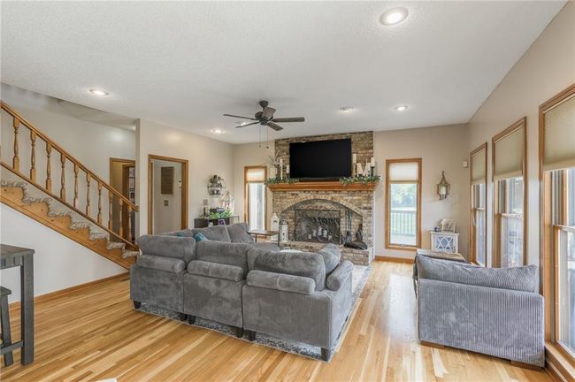 Living room with a ceiling fan, baseboards, light wood finished floors, stairs, and a brick fireplace | Image 39
