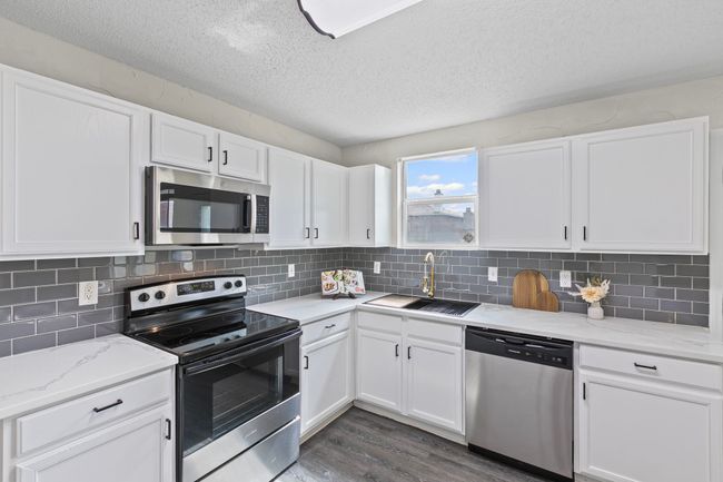 Kitchen with stainless steel appliances, dark wood-style floors, white cabinets, a textured ceiling, and light stone counters | Image 8