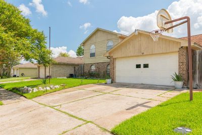 This is a two-story suburban home featuring a sizable two-car garage with a basketball hoop, a well-maintained front lawn, and mature trees offering shade and curb appeal. | Image 3