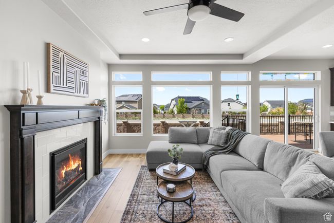 Living area with a fireplace, a tray ceiling, ceiling fan, and light wood-style floors | Image 5