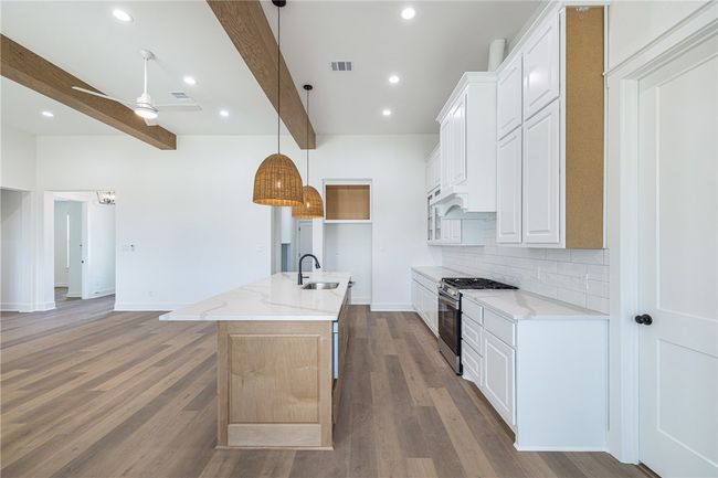 Kitchen with stainless steel gas range, white cabinets, and a kitchen island with sink | Image 10