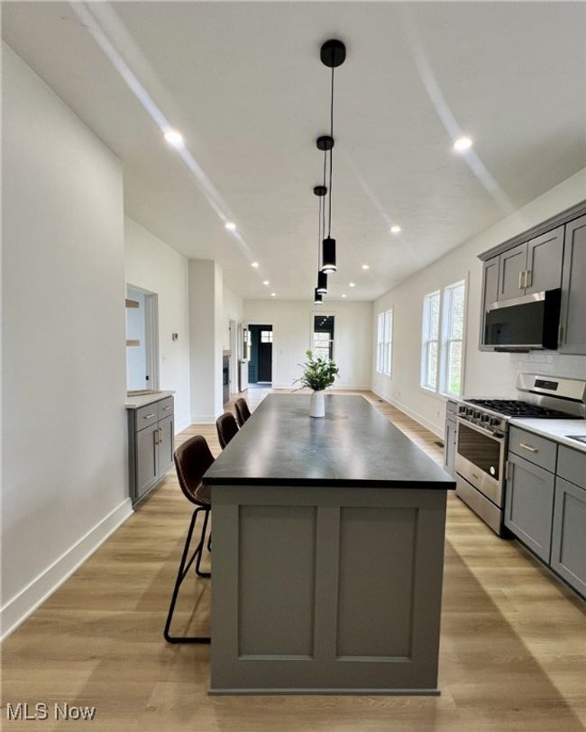 Kitchen featuring a center island, dark countertops, appliances with stainless steel finishes, light wood finished floors, and gray cabinetry | Image 10