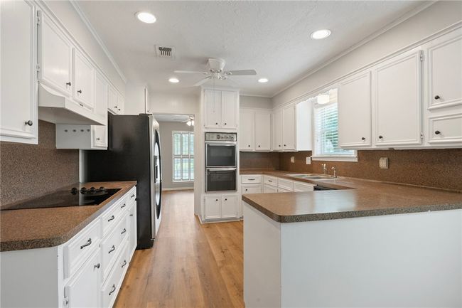 Kitchen featuring a ceiling fan, black appliances, a peninsula, light wood-style floors, and white cabinetry | Image 6