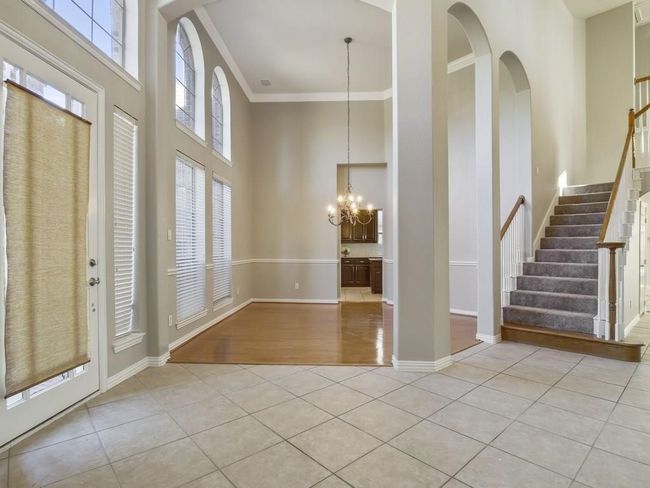 Foyer featuring a high ceiling, light tile patterned flooring, ornamental molding, a chandelier, and stairs | Image 4