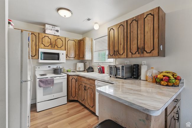 Kitchen featuring light wood finished floors, light countertops, a sink, white appliances, and a peninsula | Image 17