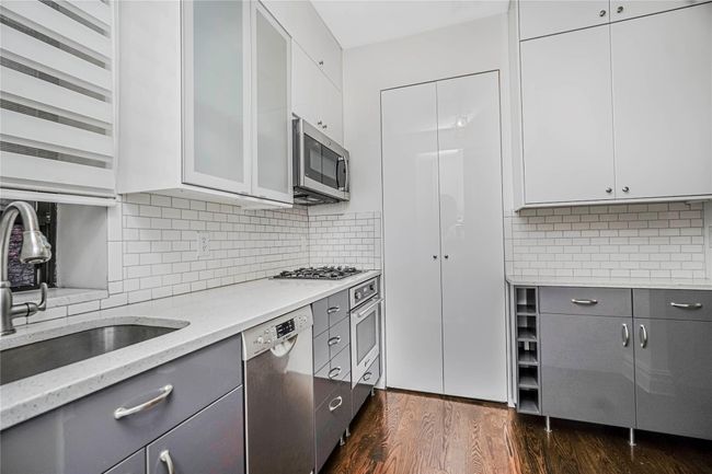 Kitchen with appliances with stainless steel finishes, gray cabinetry, dark wood-type flooring, light stone counters, and tasteful backsplash | Image 14