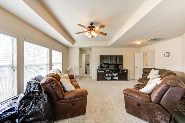 This spacious living room features large windows for natural light, cozy brown leather sofas, and a ceiling fan. It offers a comfortable area for relaxation and entertainment, with a TV and ample seating. | Image 27