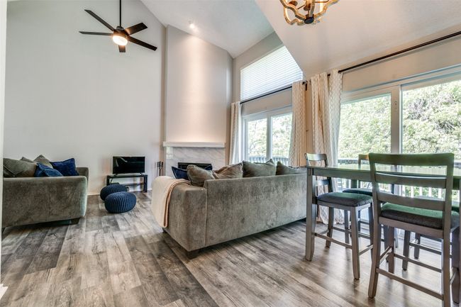 Living area with high vaulted ceiling, a chandelier, wood finished floors, a premium fireplace, and a ceiling fan | Image 6