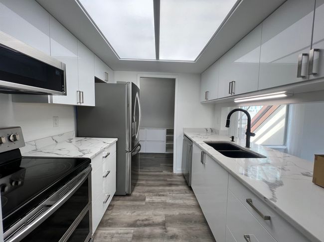 Kitchen featuring appliances with stainless steel finishes, white cabinets, light wood finished floors, and light stone counters | Image 14