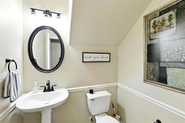 Stylish half bath located just off the family room, featuring a pedestal sink, framed mirror, updated lighting, and decorative wall trim. | Image 12
