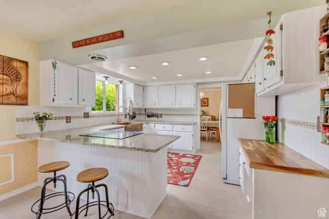 Kitchen featuring a peninsula, electric cooktop, white cabinetry, decorative backsplash, and light stone counters | Image 12