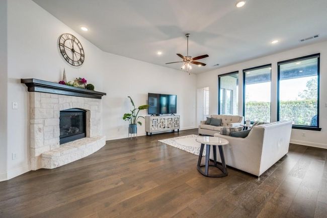 Living area with ceiling fan, dark wood finished floors, baseboards, a stone fireplace, and recessed lighting | Image 5