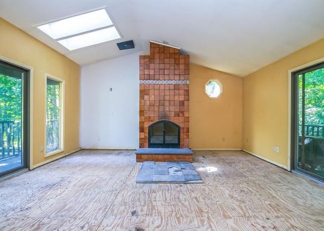 Unfurnished living room with vaulted ceiling with skylight and a tiled fireplace | Image 13