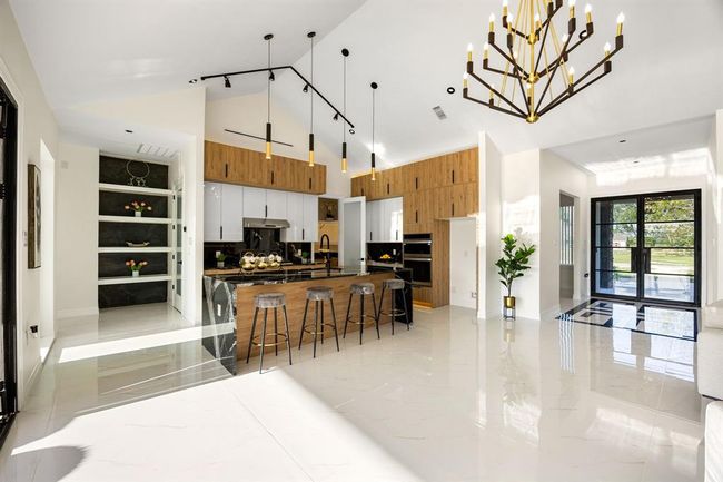 This breathtaking open-concept kitchen dazzles with soaring vaulted ceilings, striking modern lighting, and a seamless blend of natural wood and sleek finishes. Elegant black accents and high-gloss tile flooring complete the luxurious, contemporary design. | Image 37